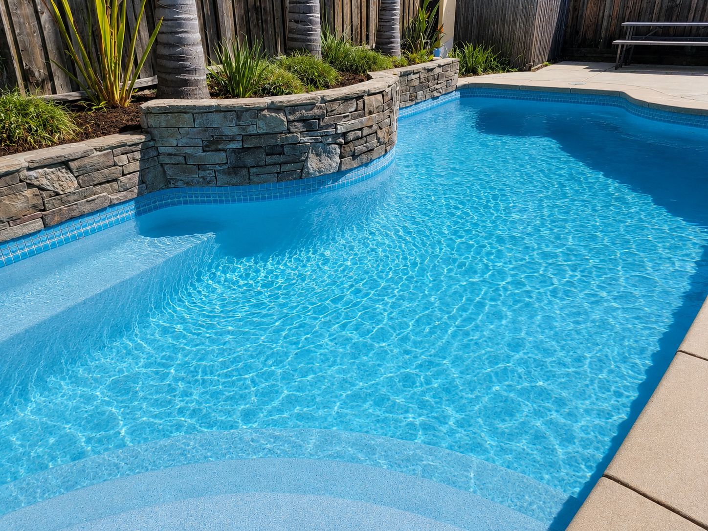 Clean backyard swimming pool with clear blue water and stone landscaping by The Goods Pool Service LLC